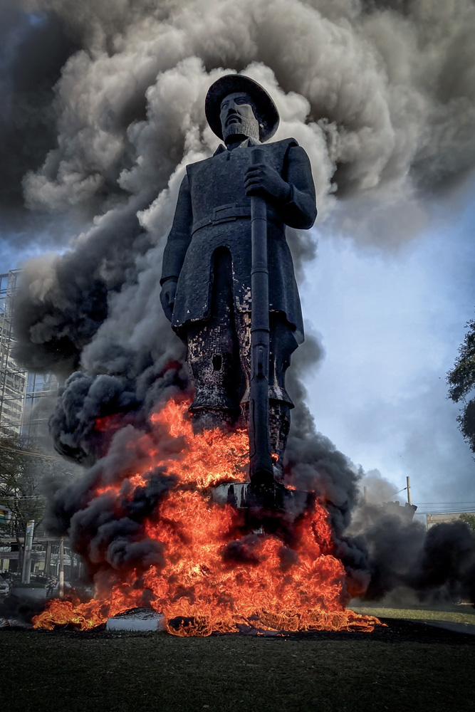 estátua de borba gato com labaredas de fogo na base e pernas com fumaça preta saindo da estrutura