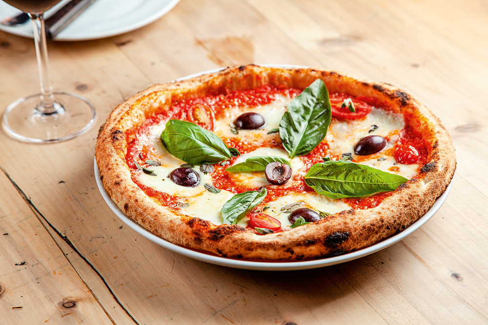 Pizza margherita com azeitona preta sobre mesa de madeira.