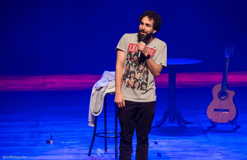 Imagem mostra Murilo no palco, segurando microfone.