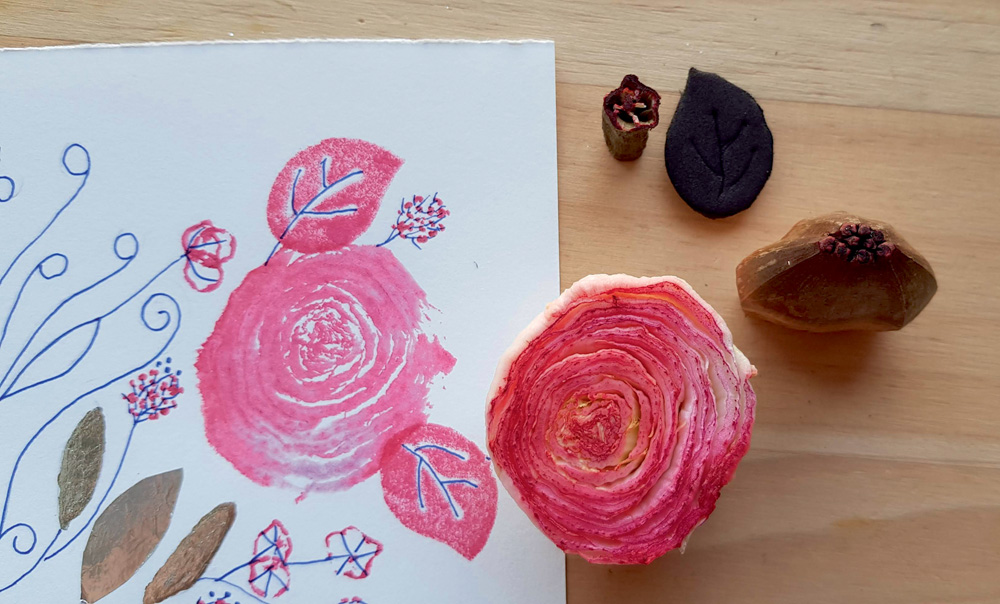 Uma folha de papel tem desenhos de folhas e rosas. Uma rosa real está do lado da folha