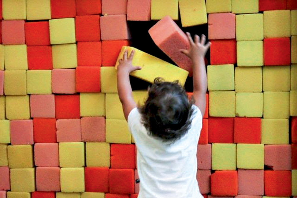Criança monta uma parede de blocos amarelos, vermelhos e rosas