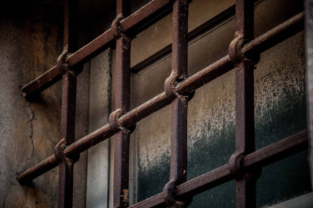 Imagem mostra grades de prisão na frente de janela fechada