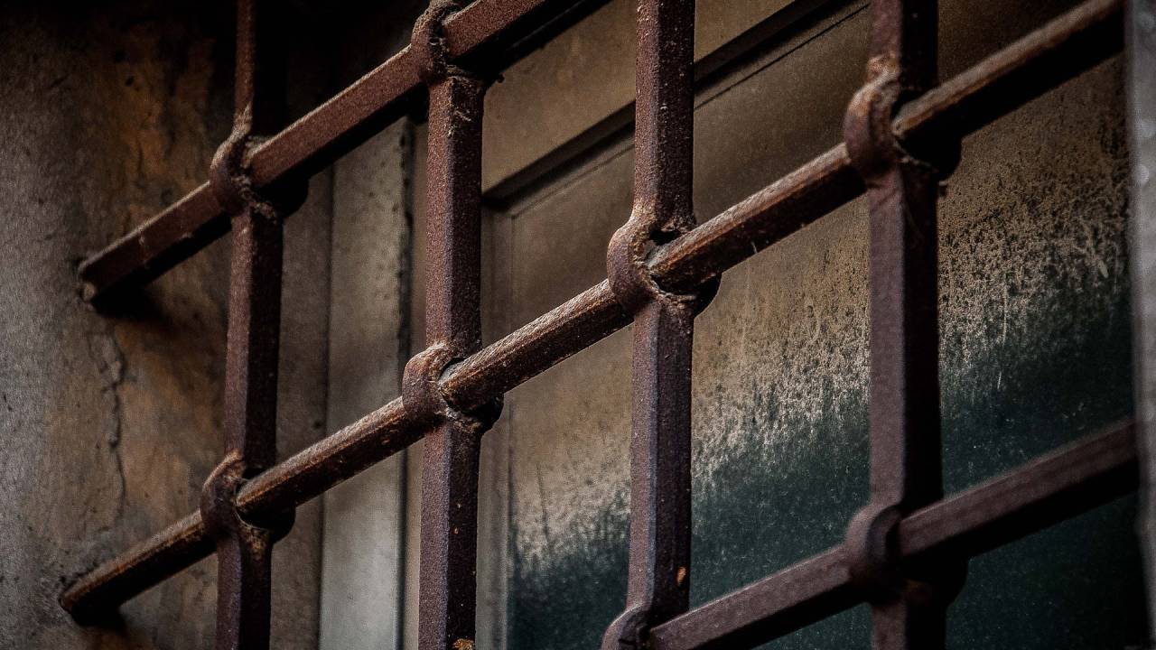 Imagem mostra grades de prisão na frente de janela fechada