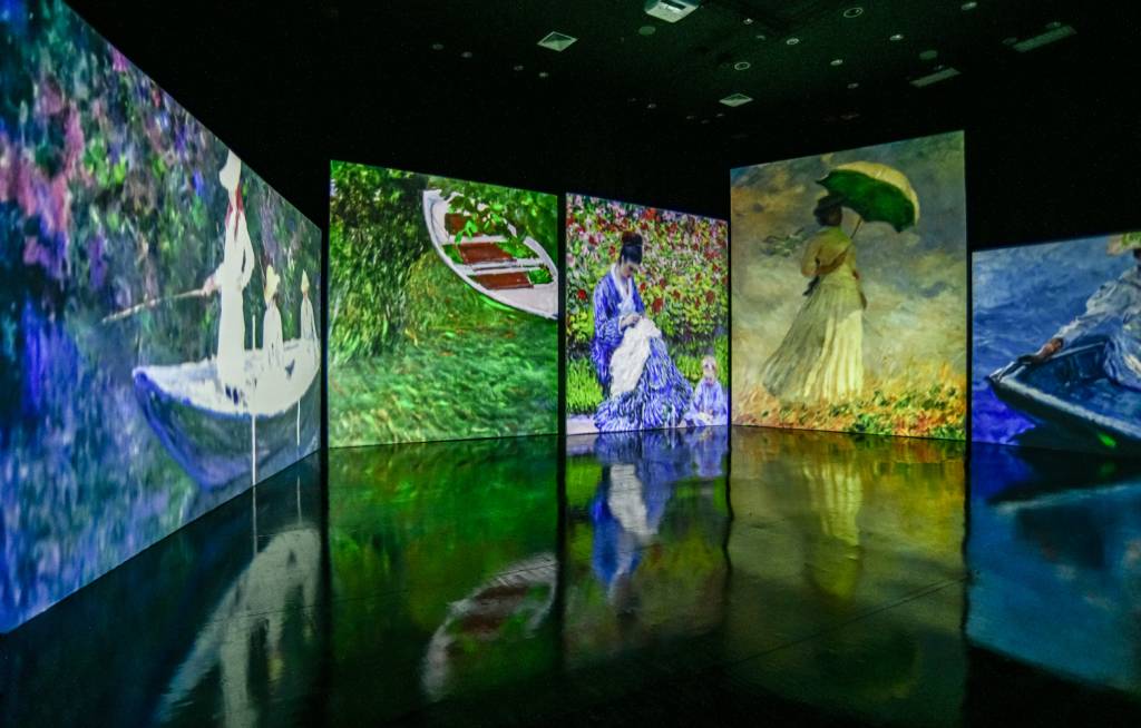 Obras de Monet projetadas na parece em sala de exposição com chão preto.