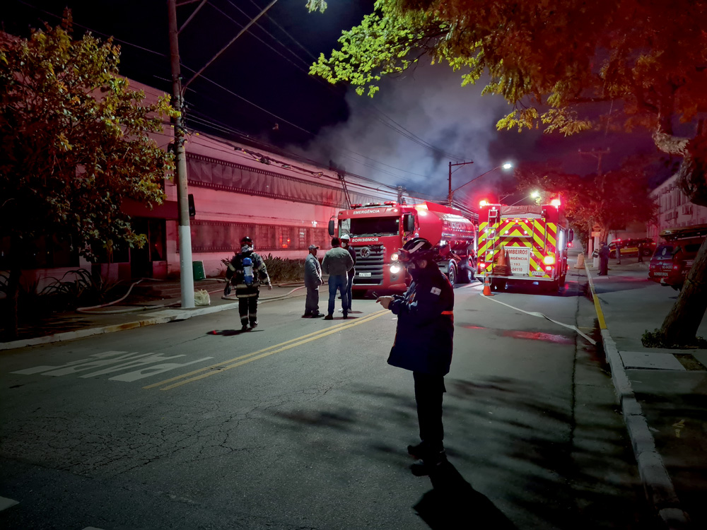 Foto mostra um caminhão do corpo de bombeiros, à noite, com oficiais trabalhando, em frente a um prédio