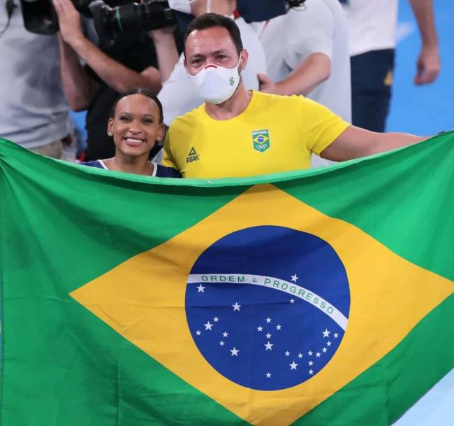 Rebeca e seu técnico, Chico Porath, com a bandeira do Brasil na frente