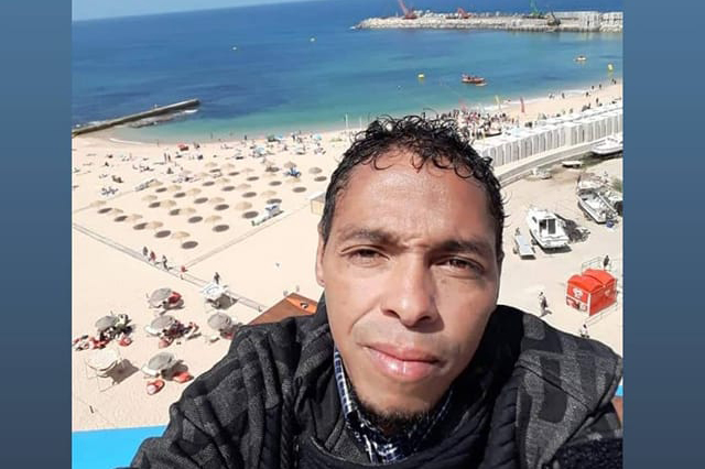 Imagem mostra selfie de Eliseu, ele usa jaqueta e, ao fundo, aparece praia em Portugal