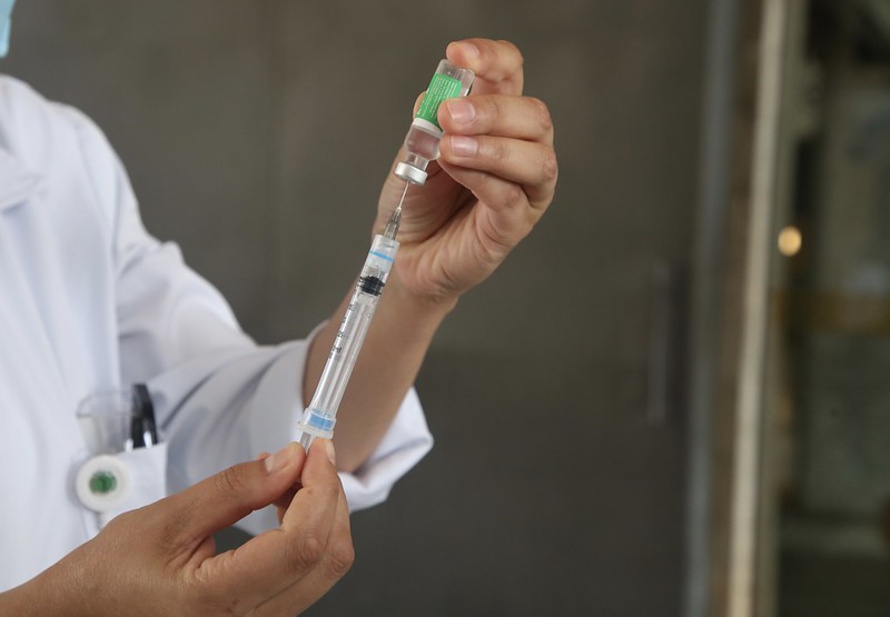 Imagem mostra enfermeira retirando dose de vacina de fraco com seringa