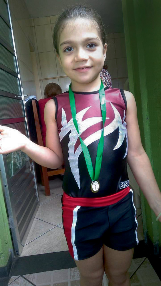 A imagem mostra Rafaelly, em pé, com uma medalha e seu uniforme de ginasta.