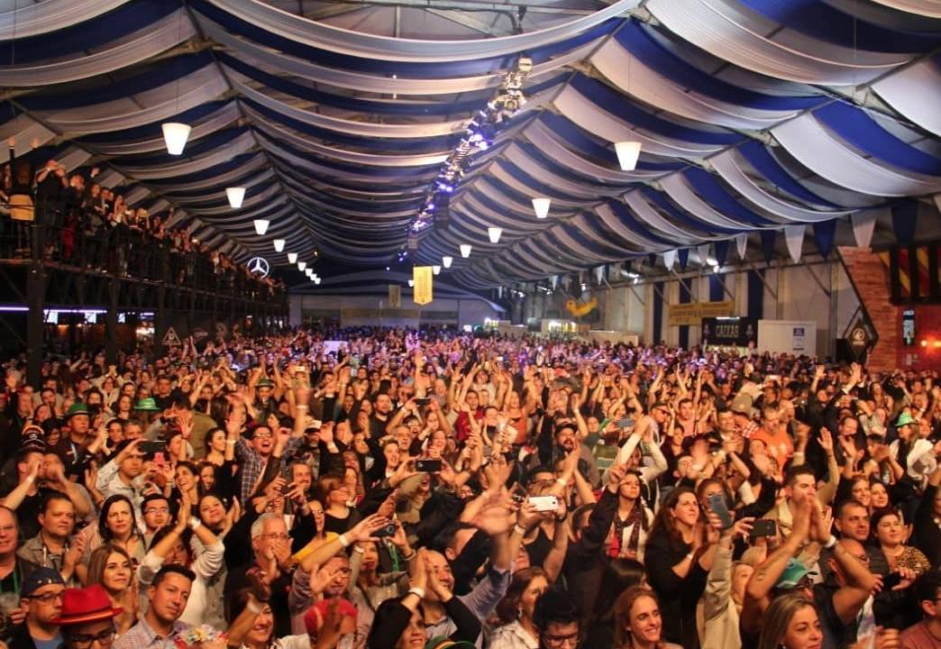 Oktoberfest 2019: pessoas de costas brindando canecas de chope com cantora no palco