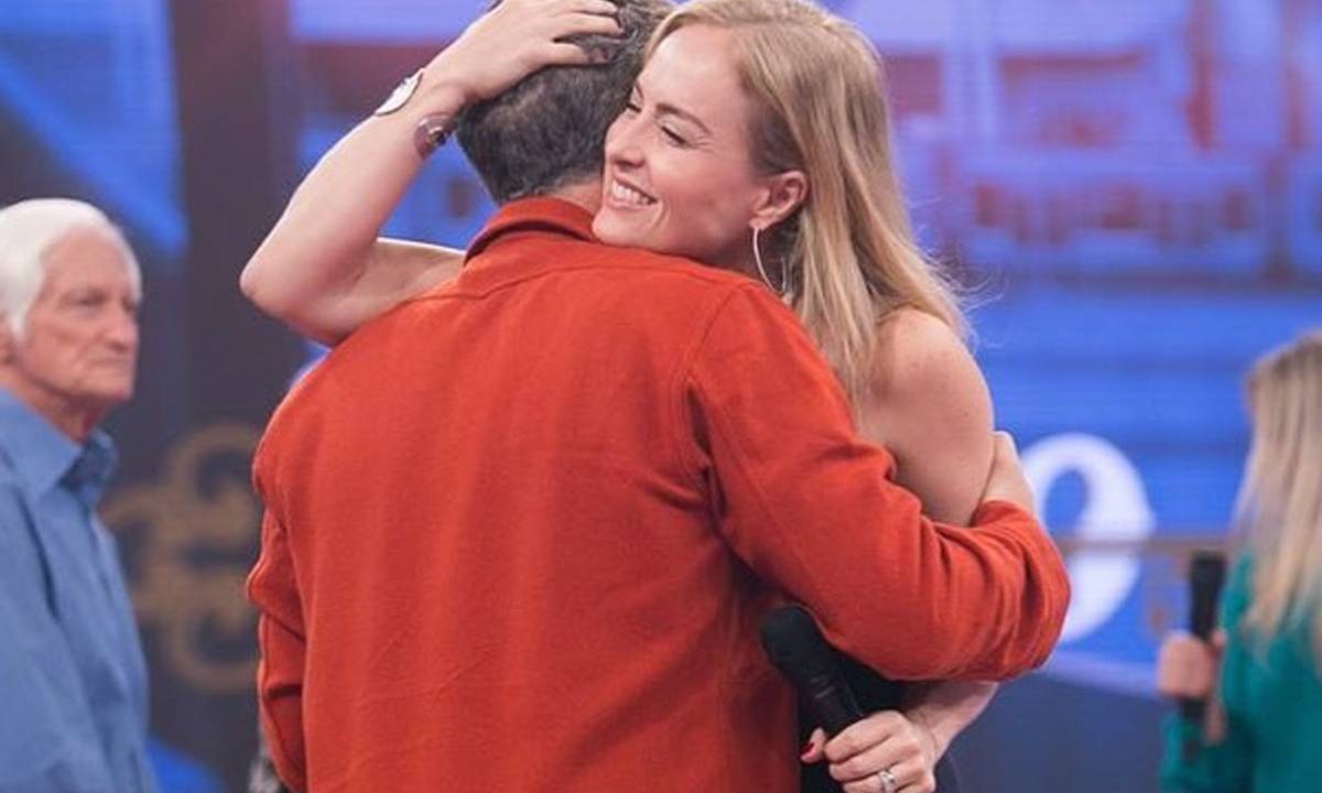 Angélica abraça Luciano Huck, que aparece de costas vestindo camisa vermelha.