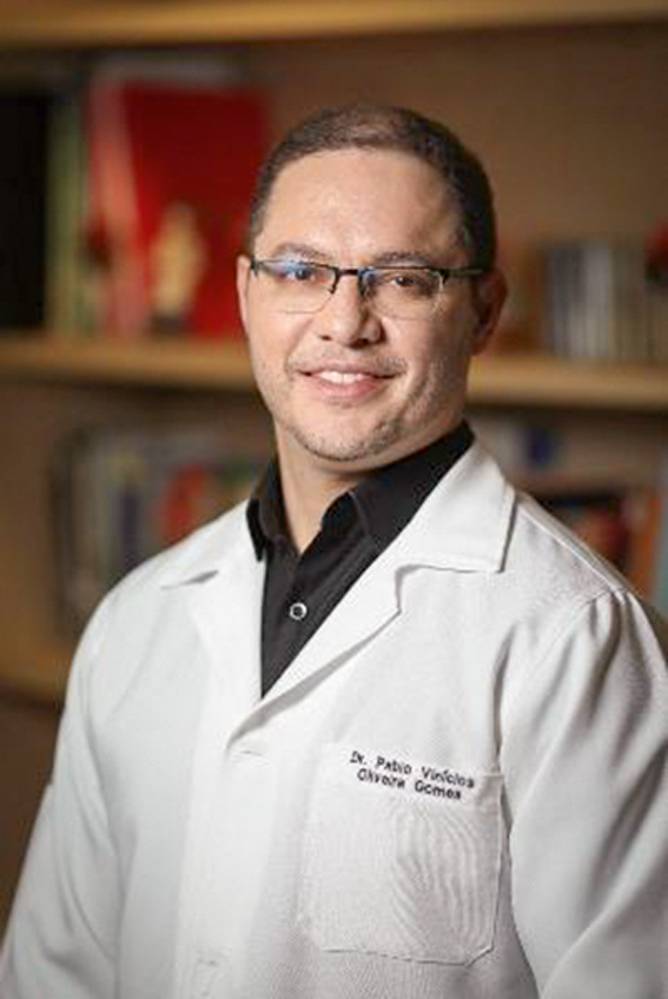 DR.-PABLO-VINICIUS-sem-moderação-sem-medicação-a-tal-felicidade.jpg dr. pablo vinícius posando para a foto sorrindo com jaleco de doutor. ele tem cabelo ralo, testa grande e usa óculos