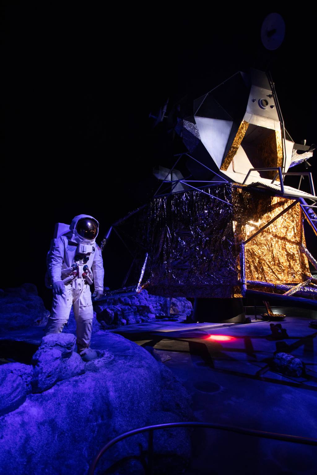 Foto mostra astronauta e nave parados em cenário azul.