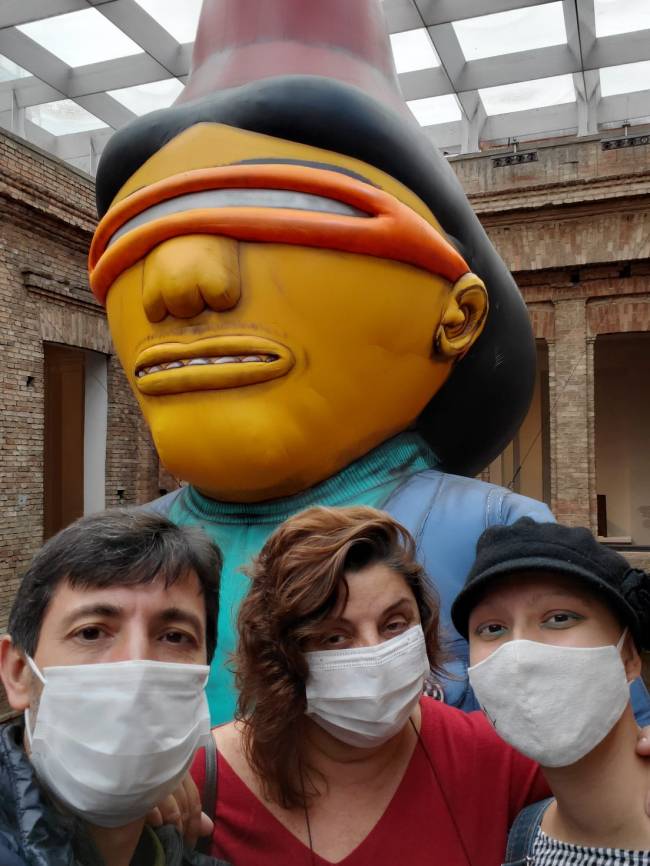 Família Angueira em passeio cultural: a partir da esquerda, Victor, Lourdes e a filha Victoria. A foto mostra os três de máscara posando em frente a uma escultura d'Os Gêmeos.