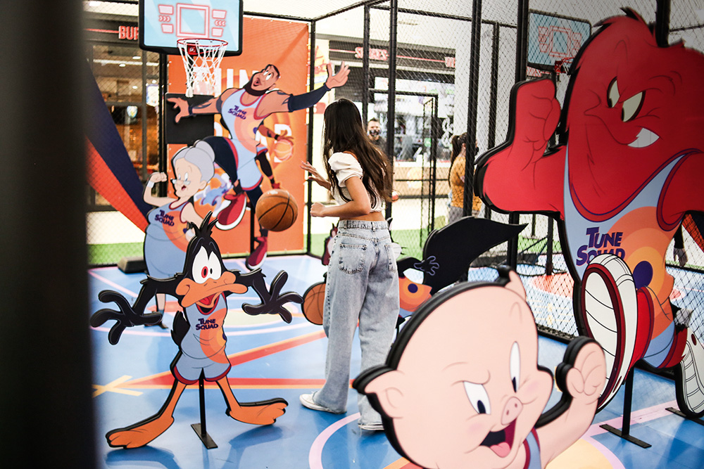 Menina está jogando basquete em uma miniquadra com vários bonecos dos personagens de Looney Tunes