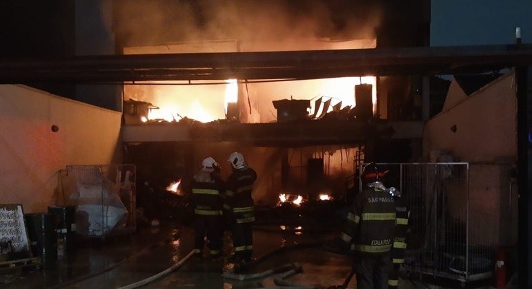 Imagem de casa incendiada e bombeiros em frente.