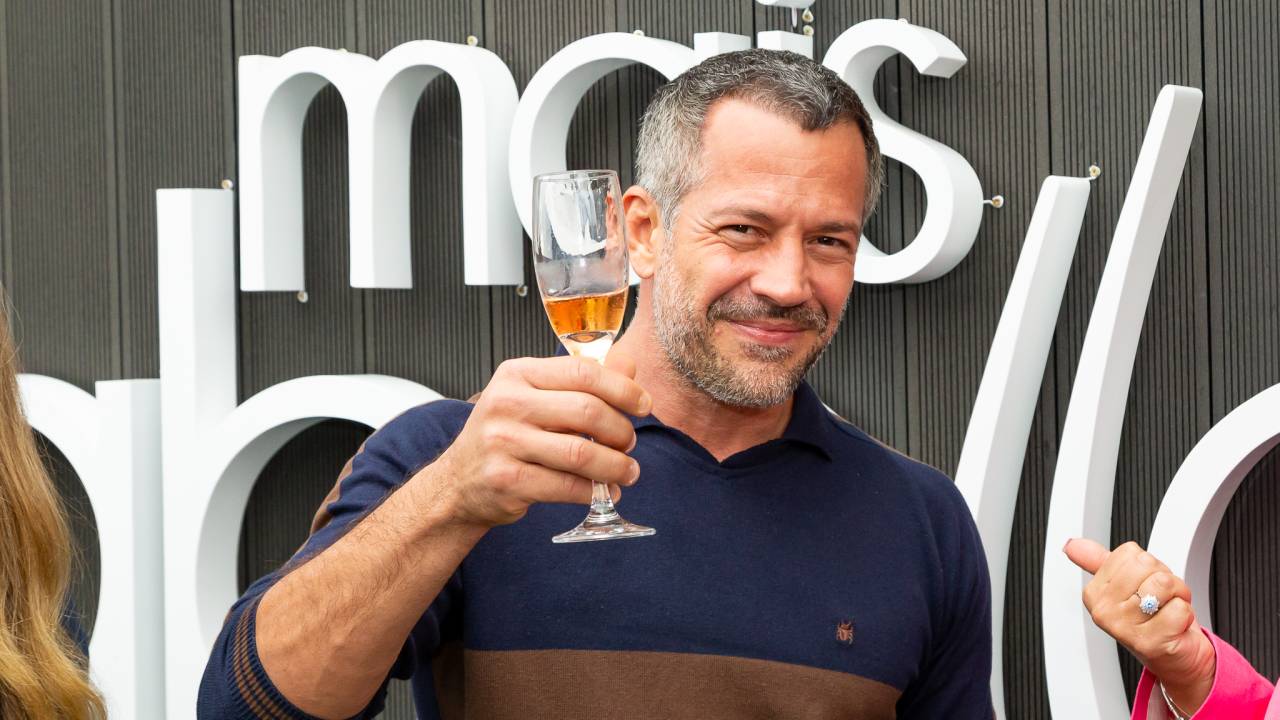 O ator Malvino Salvador ergue taça de champanhe e sorri para a câmera.