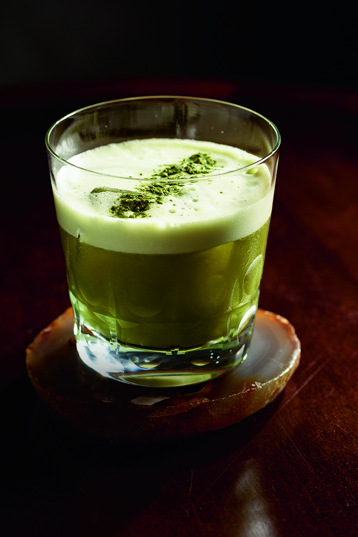 Drinque de cor verde com espuma branca em copo baixo de vidro sobre porta-copos.