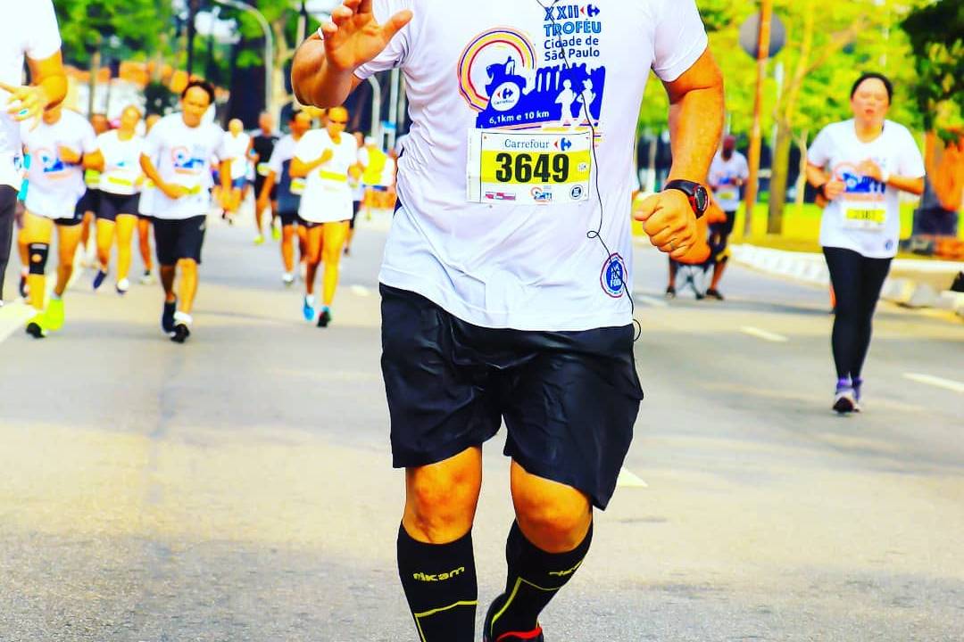 A imagem mostra Rodolfo, em uma maratona, correndo em uma rua. Ele está de boné e roupas esportivas.
