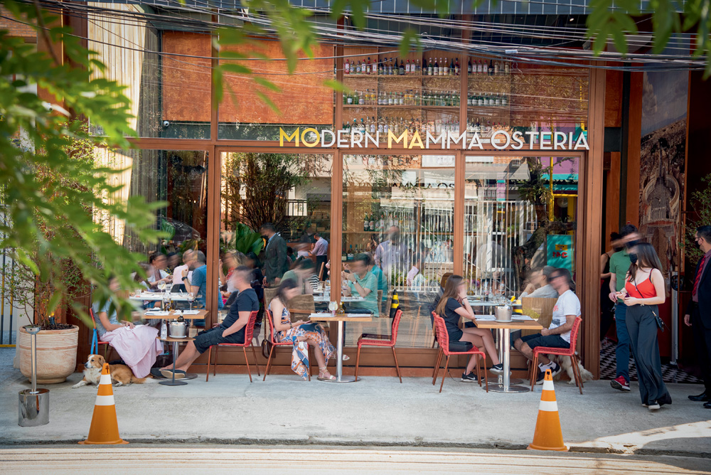 Fachada envidraçada do restaurante Moma Modern Mamma Osteria em Pinheiros com pessoas sentadas em mesas na calçada.
