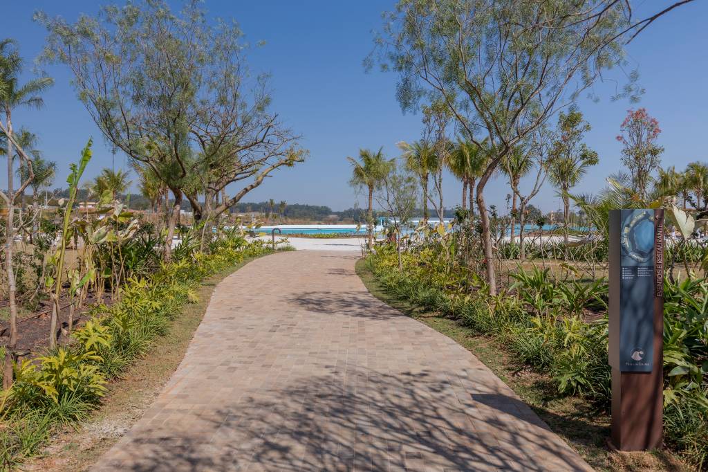 Foto mostra pedaço da praia artificial com ondas e areia em condomínio de luxo.