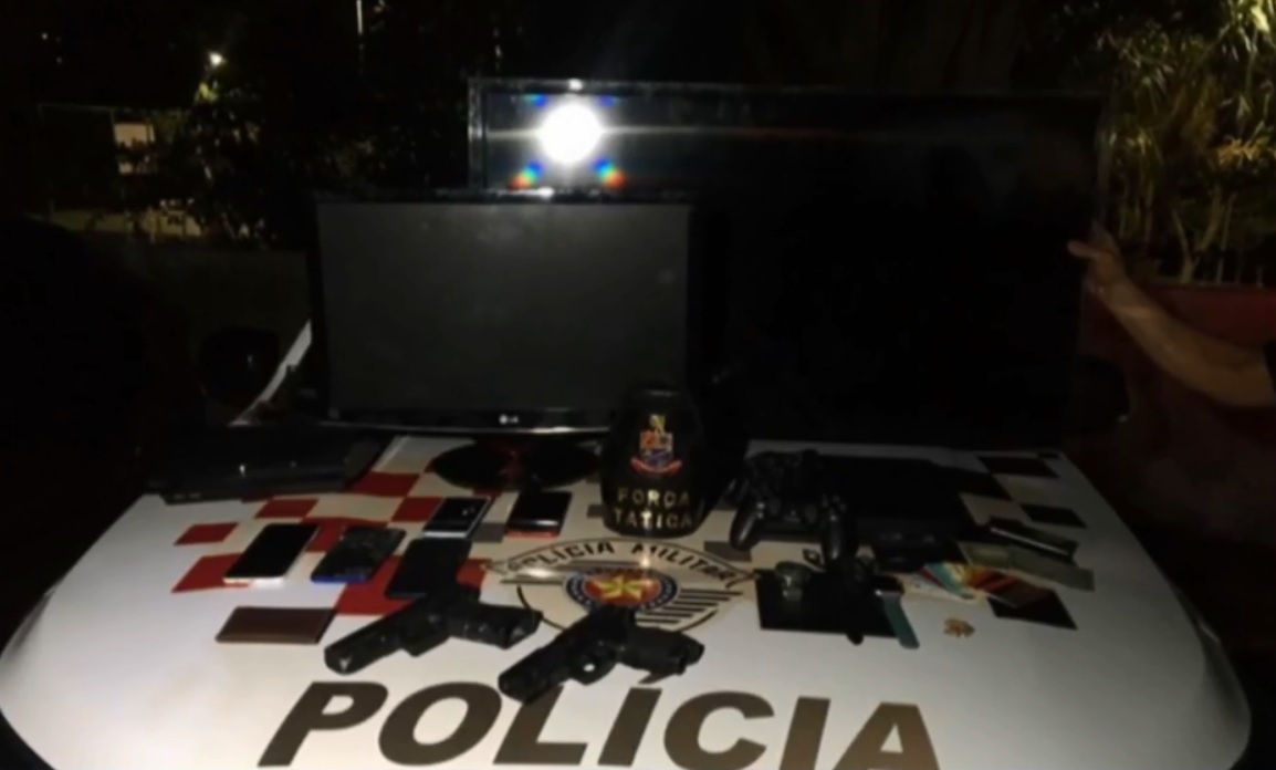 A imagem mostra o capo de um carro da polícia com diversos itens, como televisão, celular, armas, monitores, entre outros.
