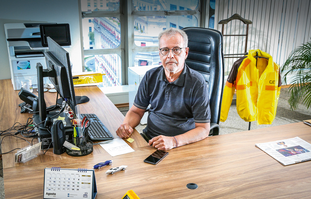 A imagem mostra Ricardo Teixeira em seu gabinete. Ele está sentando em frente ao seu computador, e atrás, há uma jaqueta típica dos guardas da CET.