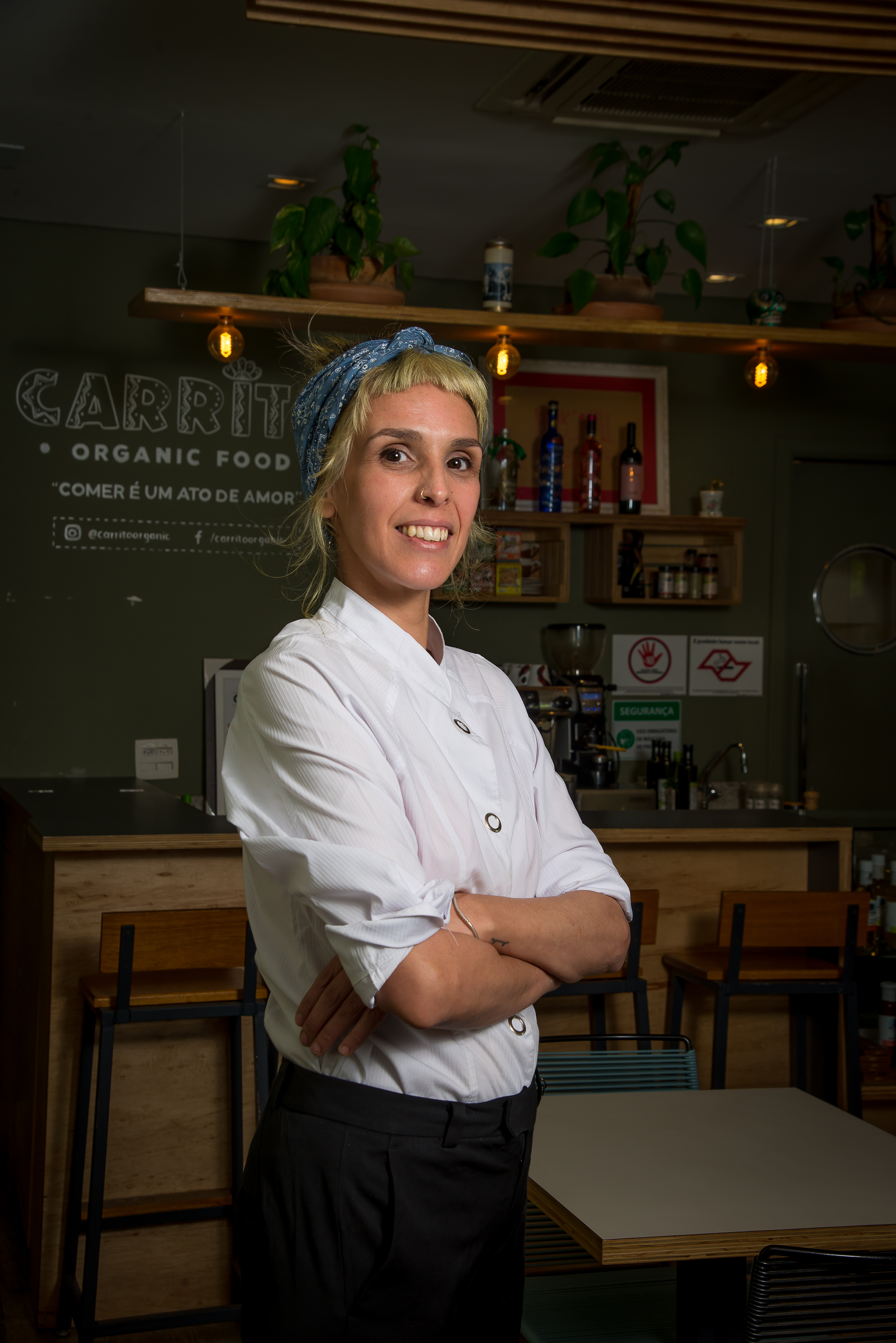 Imagem mostra Camila, com lenço no cabelo e braços cruzados, diante do saguão do restaurante Carrito