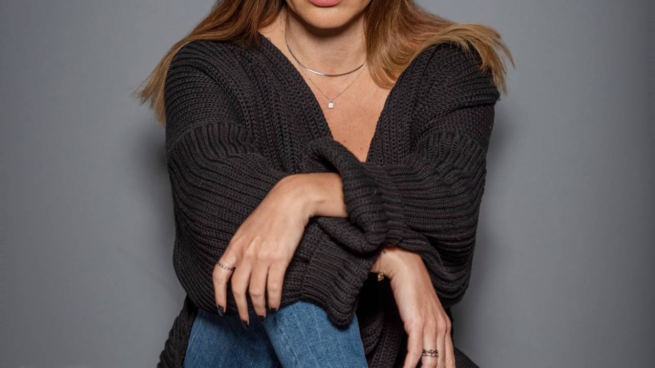 Roberta Alonso, diretora e atriz, aparece sentada no chão com perna cruzada. Veste camiseta preta e jeans.
