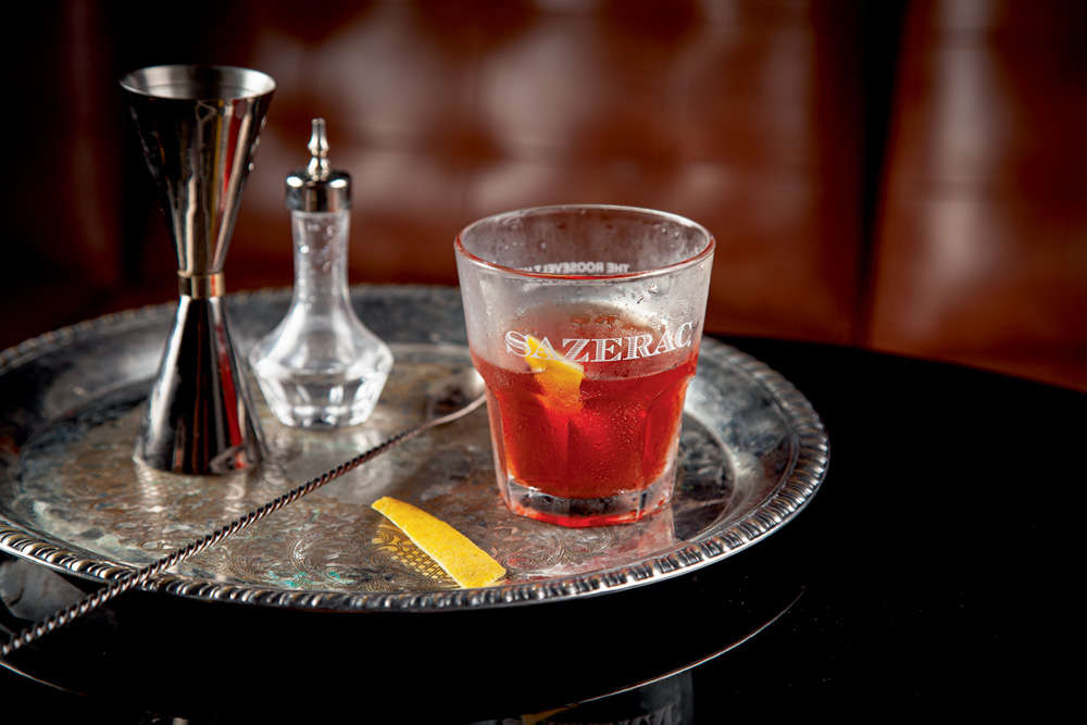 Drinque vermelho em copo de vidro sobre bandeja de preta em cima de mesa prata.