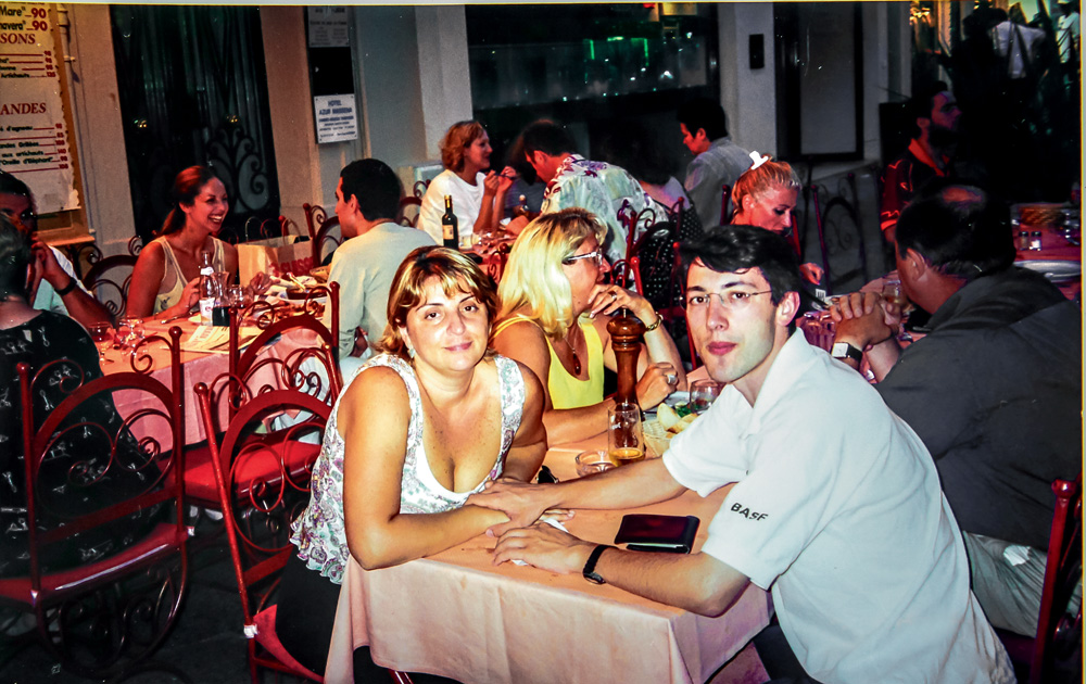 foto antiga de victor e lourdes posando para a foto em um restaurante em porto seguro. eles estão encostando um no outro com os braços, que estão sobre a mesa