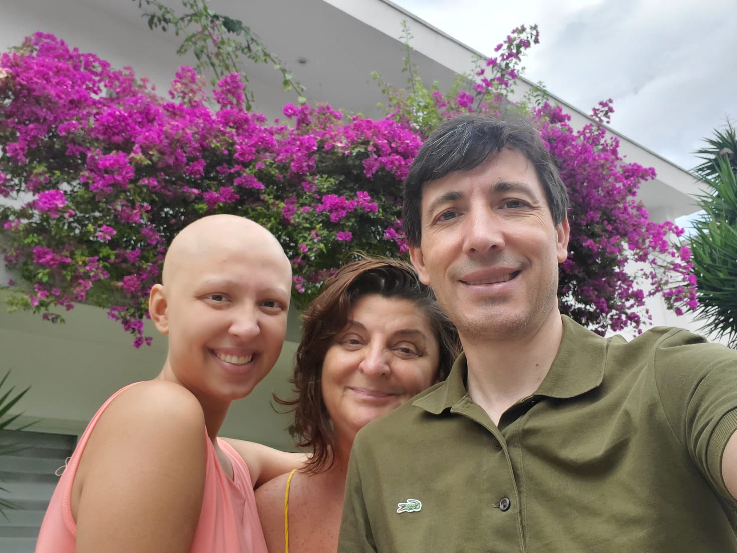 A filha Victoria ao lado dos pais Lourdes e Victor. Os três aparecem lado a lado em frente a uma plantação de flores roxas.