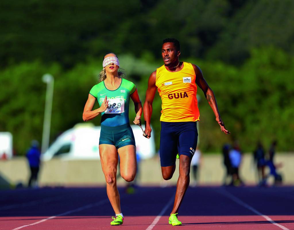 Uma atleta com uma venda no rosto corre na pista com seu guia