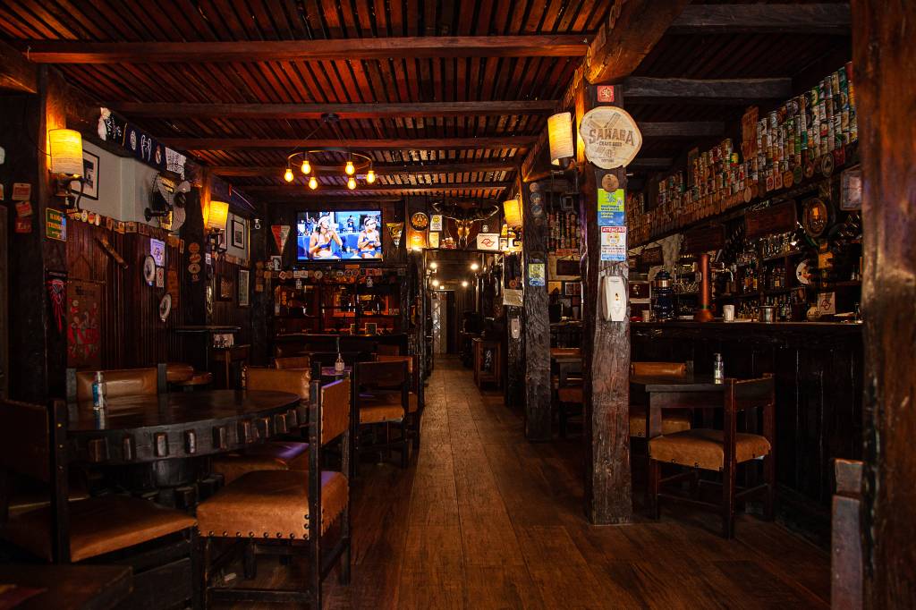Salão do bar Zur Alten Mühle com paredes de madeira cobertas por bolachas de chope e mesas de madeira com cadeiras com estofaos de couro.