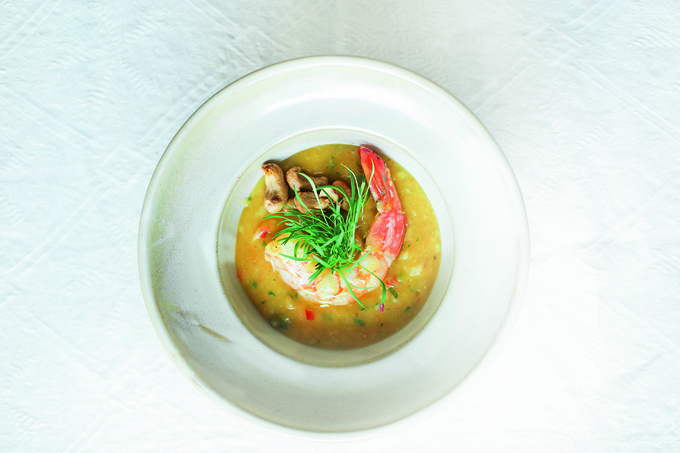 Em um prato fundo de cor branca, bobó servido com camarão e castanhas de caju no topo.