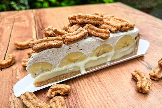 Fatia de churroffee, torta com massa, creme, rodelas de banan e chantili coberta por cereais em forma de minichurros.