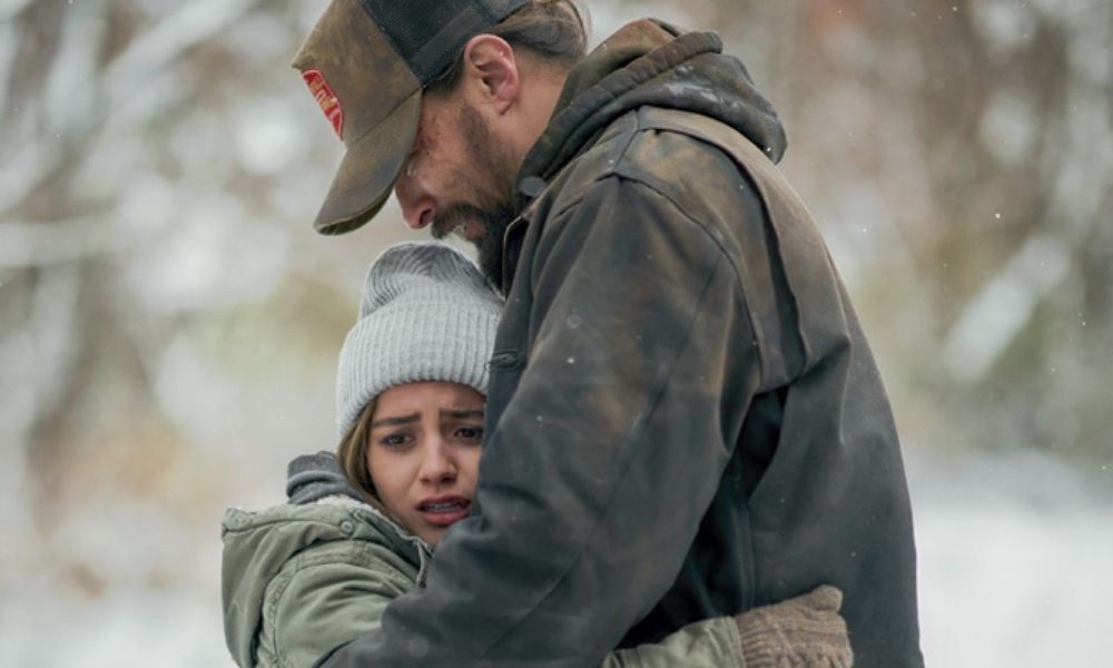 A imagem mostra Jason e Isabela abraçados, completamente agasalhados em meio a um ambiente coberto com neve.