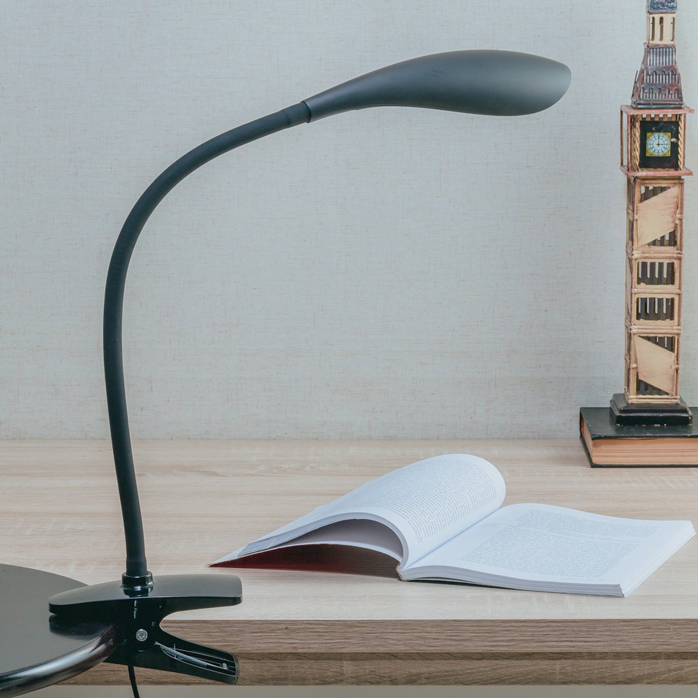 Uma luminária preta simples em cima de uma mesa. Está iluminando um livro