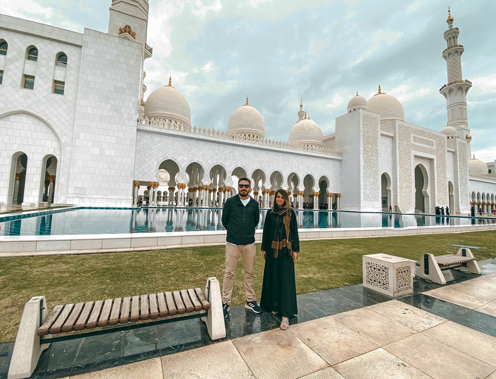 tati e gabriel posando para a foto com mesquita ao fundo, em abu dhabi