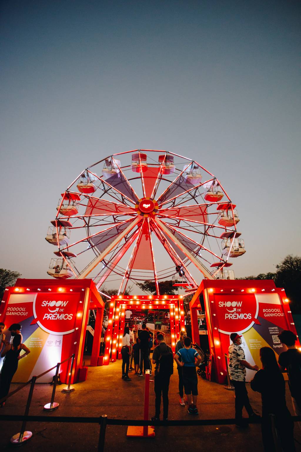 vista do chão de roda-gigante do ifood com fila e cabines de sorteio de prêmios à frente da atração