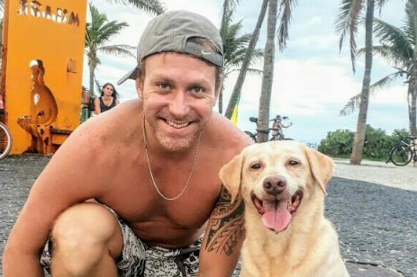 Imagem mostra Sergio sorrindo de boné, em calçadão de praia, ao lado de cachorro