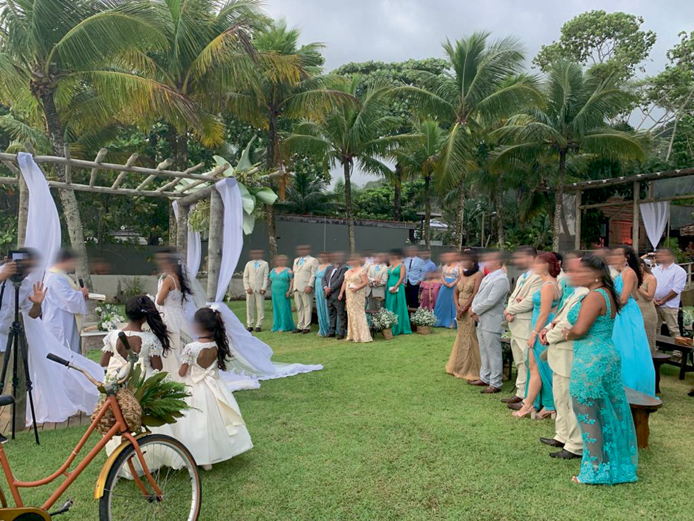 Foto mostra uma cerimônia de casamento em um gramado na praia. Convidados observam o altar