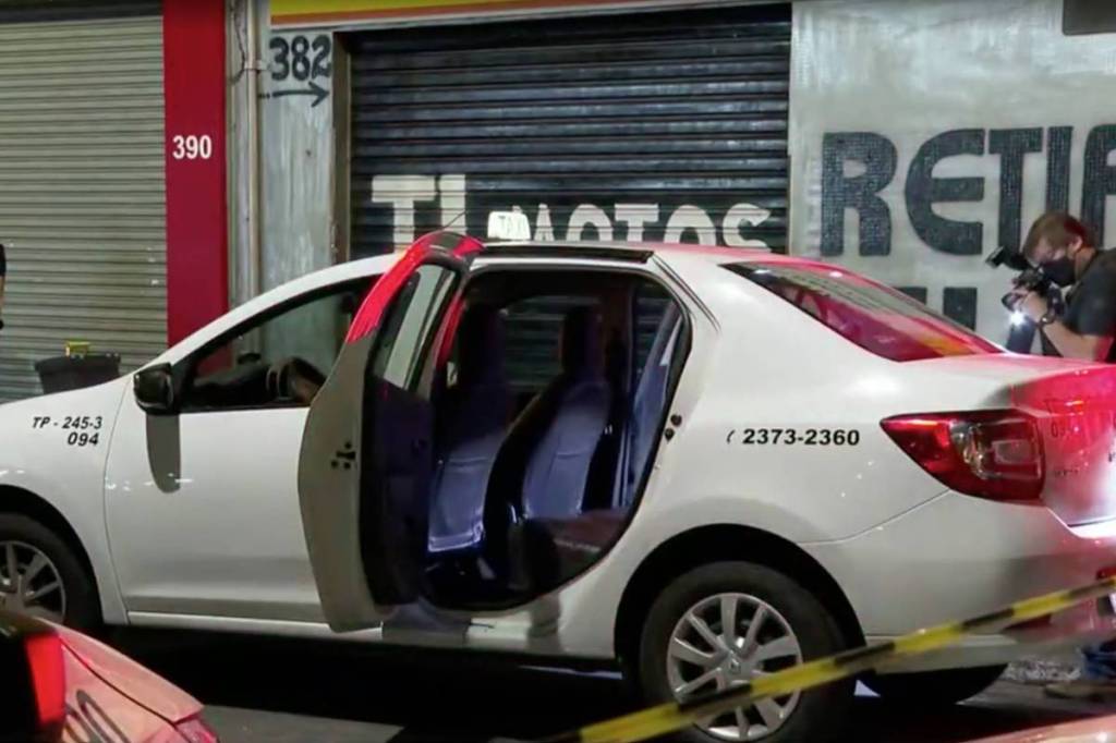 A imagem mostra um Táxi interceptado por grupo para socorrer homens esfaqueados; o veículo está com a porta traseira aberta