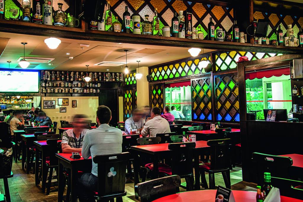 Ambiente do Bar Léo decorado por mosaicos de vidro e garrafas à vista
