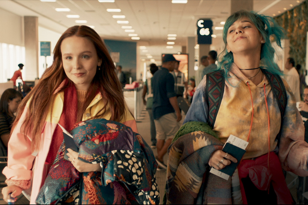 A imagem mostra Larissa e Thati em aeroporto andando com suas malas e felizes.
