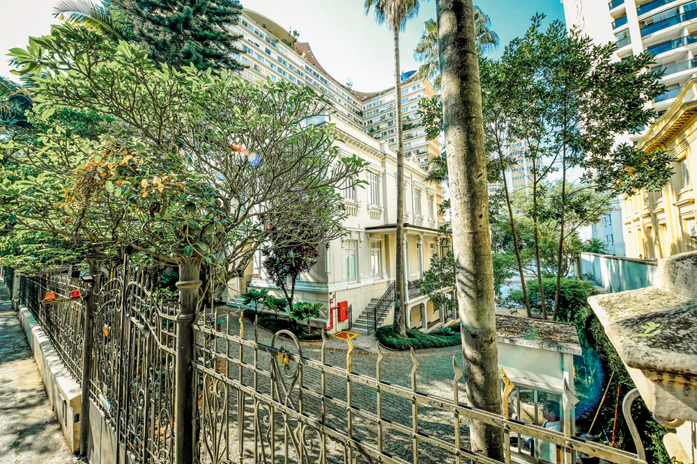 Foto lateral do casarão da Mitra Arquidiocesana de São Paulo, no Higienópolis. Há árvores cercando a construção
