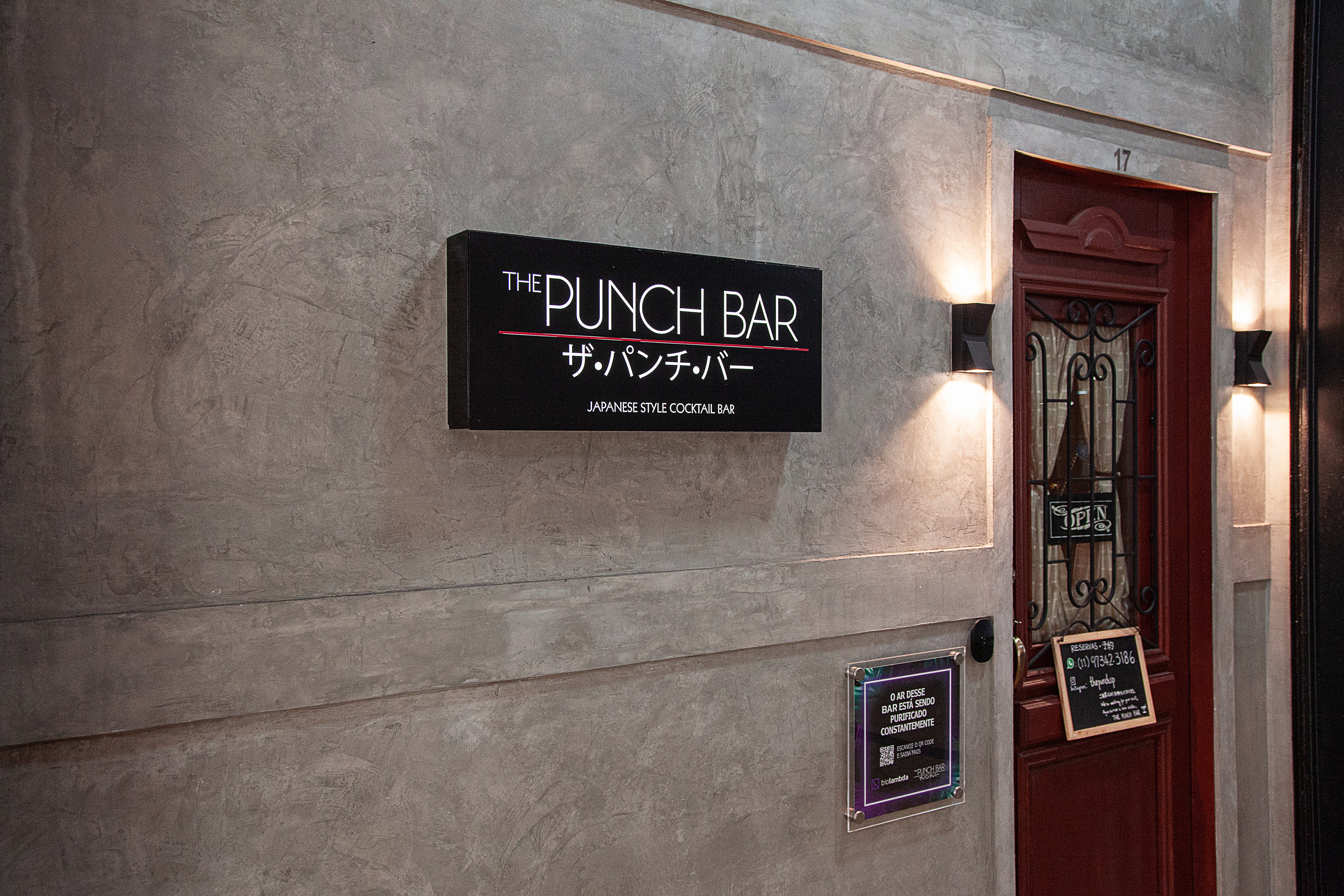 Fachada do The Punch Bar de concreto ao lado da porta de madeira.