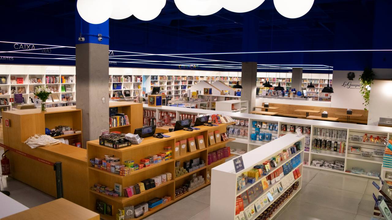 Livraria da Vila no Pátio Higienópolis. Foto exibe prateleiras de madeira e corredores da livraria bem iluminada com parede azulada.