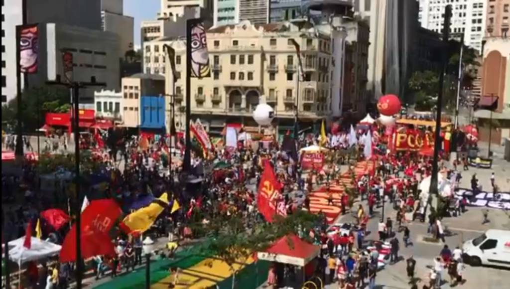 A imagem mostra o Anhangabaú cheio de pessoas com bandeiras vermelhas, verdes e a amarelas.