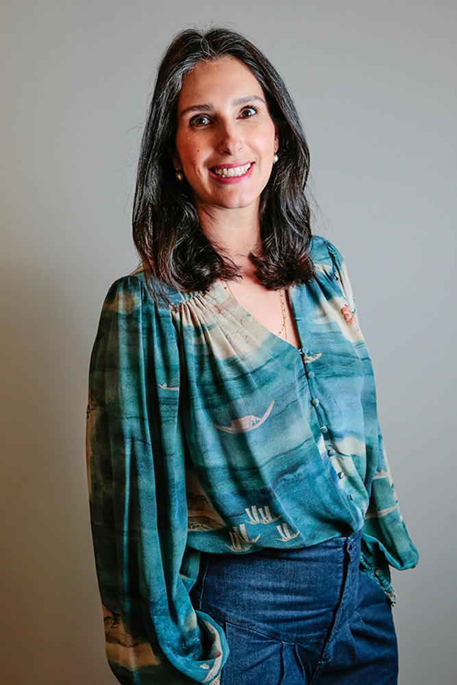 Maria Fernanda Quartiero sorrindo em estúdio. ela está utilizando uma blusa azul